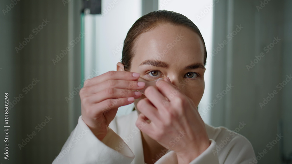 Woman applying gel patches under eyes for skincare routine at home portrait. Woman applying gel patches under eyes for skincare routine at home portrait.