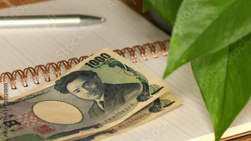 A Japanese man holding money in his hand and writing down his income and expenses in a notebook. A Japanese way of saving and controlling a household budget called kakeibo. Japan finances
