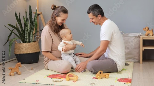 Parents and newborn baby. Caucasian family father and mother kissing and hugging beautiful infant child while sitting on colorful couple in living room