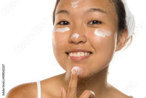 Beautiful young Asian woman applying cosmetic cream treatment on her face