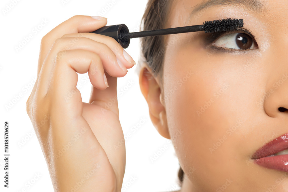 Closeup portrait of a young Asian woman applying mascara.