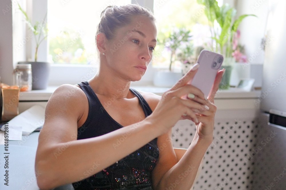 In a bright and cheerful kitchen setting, a determined young woman is focused on her smartphone device