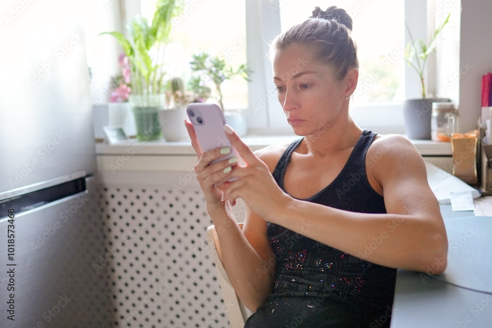 In a bright and cheerful kitchen setting, a determined young woman is focused on her smartphone device In a bright and cheerful kitchen setting, a determined young woman is focused on her smartphone device
