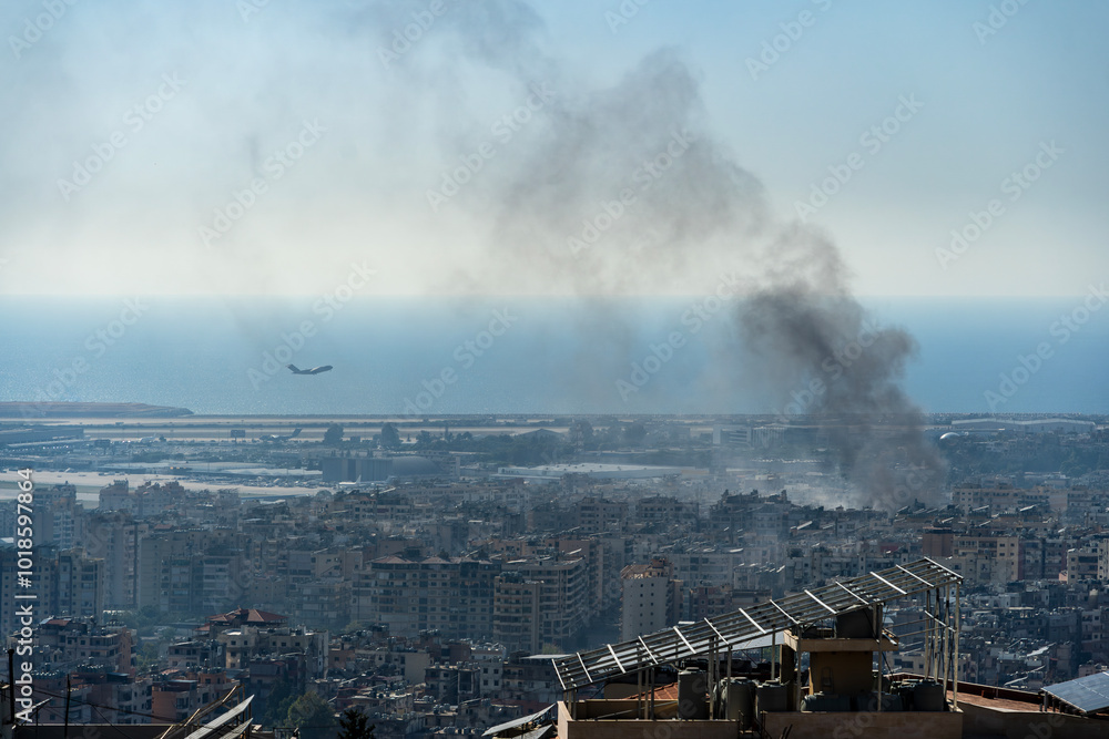 Fototapeta premium A plane taking off from Beirut International Airport as smoke rises from airstrike on Beirut southern suburbs, amid ongoing war between Hezbollah and Israel in October 2024