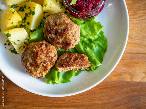 Fried meatballs, boiled potatoes, beetroots and fresh vegetables served on white plate on wooden table
