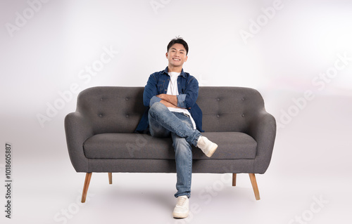 Full body image of young Asian man posing on sofa on white background