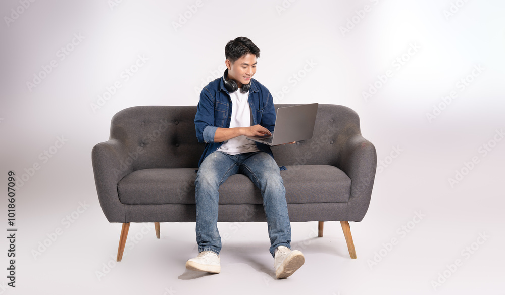 Full body image of young Asian man using laptop sitting on sofa on white background Full body image of young Asian man using laptop sitting on sofa on white background