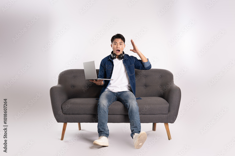 Full body image of young Asian man using laptop sitting on sofa on white background Full body image of young Asian man using laptop sitting on sofa on white background
