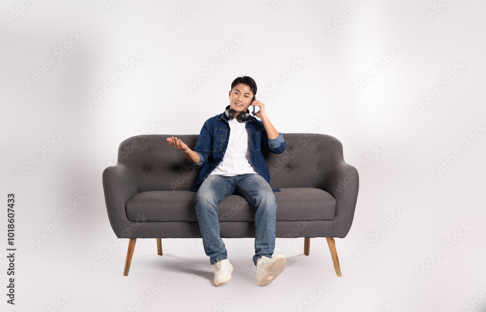 Full body image of young Asian man using phone sitting on sofa on white background Full body image of young Asian man using phone sitting on sofa on white background