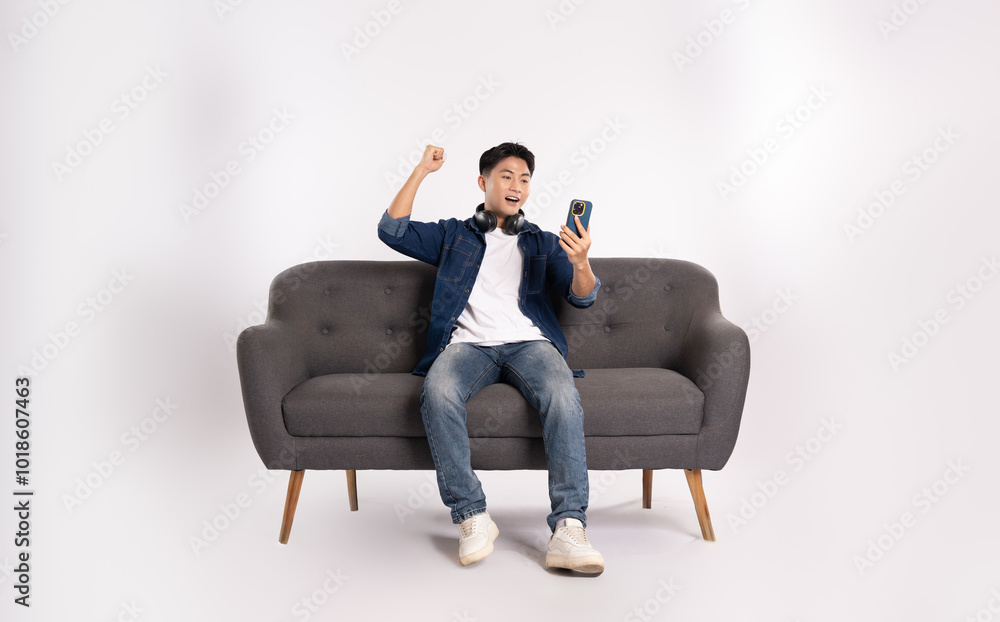 Full body image of young Asian man using phone sitting on sofa on white background Full body image of young Asian man using phone sitting on sofa on white background