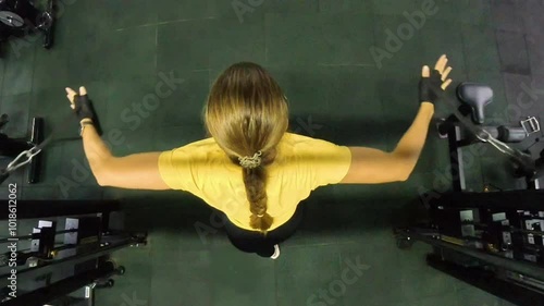 Overhead view of a Woman performing a Cable Machine Fly exercise. Her arms are extended outward as she pulls the cables, emphasizing upper body strength in the Gym. photo