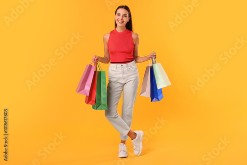 Smiling woman with colorful shopping bags on yellow background