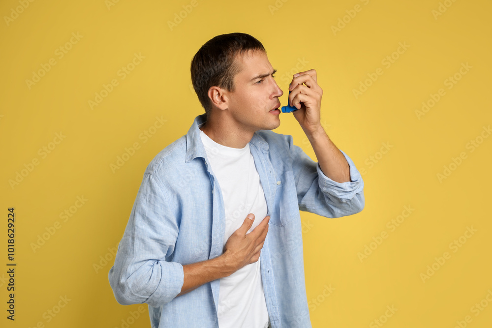 Man using asthma inhaler on yellow background Man using asthma inhaler on yellow background