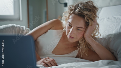 Relaxed woman watching computer online. Closeup serene girl lying on cozy bed