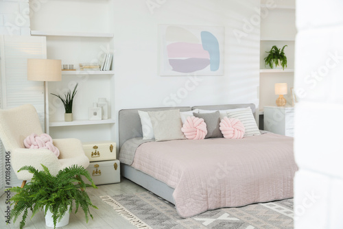 Large bed, houseplants and decorative elements in room. Stylish bedroom interior