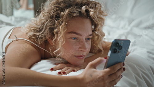 Fotografie Restful woman using mobile phone lying in bed closeup