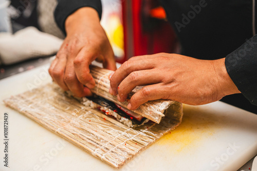 Hands skillfully rolling sushi with a bamboo mat, showing the detailed process. Great for instructional cooking content or food photography focused on sushi.