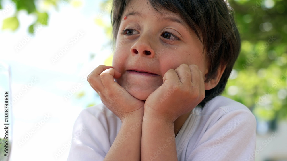 Close-up of a young boy resting his chin in his hands, gazing off to the side with a thoughtful expression, enjoying a sunny day outdoors Close-up of a young boy resting his chin in his hands, gazing off to the side with a thoughtful expression, enjoying a sunny day outdoors