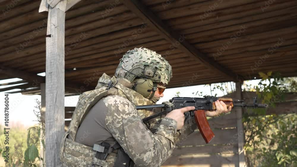 A soldier in full combat gear aims his assault rifle while taking cover ...