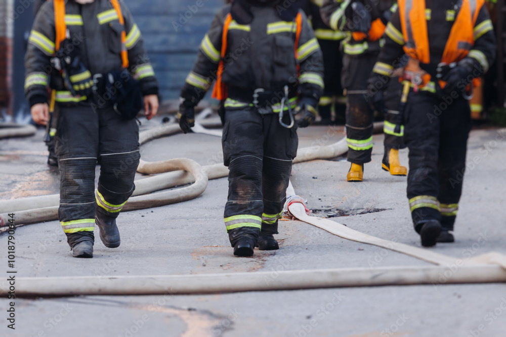 Group of fire men in uniform during fire fighting operation in the city streets, firefighters with the fire engine truck vehicle in the background, emergency and rescue, fire drill, exercise training Group of fire men in uniform during fire fighting operation in the city streets, firefighters with the fire engine truck vehicle in the background, emergency and rescue, fire drill, exercise training
