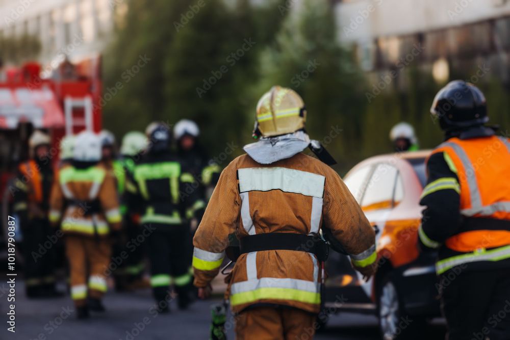 Group of fire men in uniform during fire fighting operation in the city streets, firefighters with the fire engine truck vehicle in the background, emergency and rescue, fire drill, exercise training Group of fire men in uniform during fire fighting operation in the city streets, firefighters with the fire engine truck vehicle in the background, emergency and rescue, fire drill, exercise training
