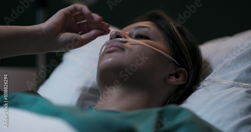Young woman lying in hospital bed with oxygen tube in her nose.