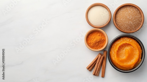 Flat lay of pumpkin recipe ingredients pumpkin puree, cinnamon, nutmeg, and brown sugar on white marble background 