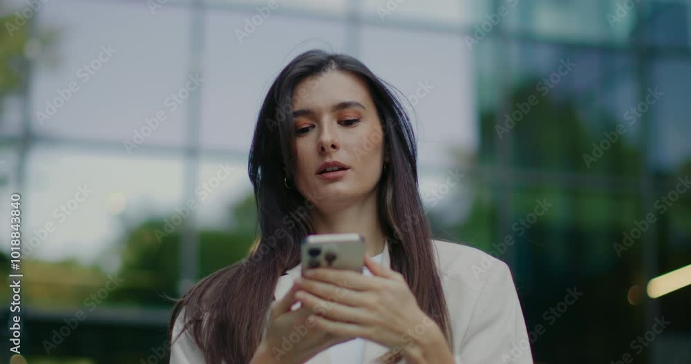 Cute Caucasian woman using her mobile device. Calling someone. Beginning conversation. Talking remotely with friend or relative after finishing working in tall business center. Manager going home. Cute Caucasian woman using her mobile device. Calling someone. Beginning conversation. Talking remotely with friend or relative after finishing working in tall business center. Manager going home.