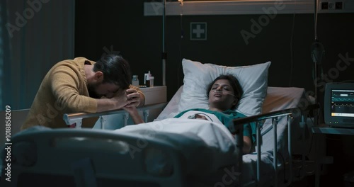 Young girl lies unconscious in a hospital bed with an oxygen tube in her nose. Beside her sits a tired-looking man.