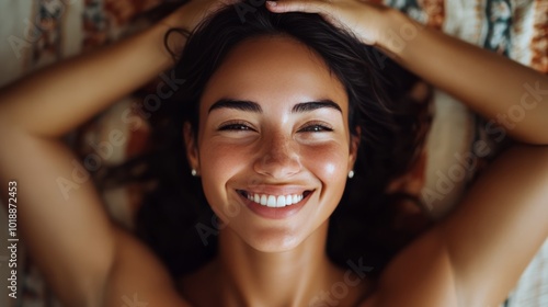 A joyful woman smiling brightly while relaxing on a colorful blanket indoors ...
