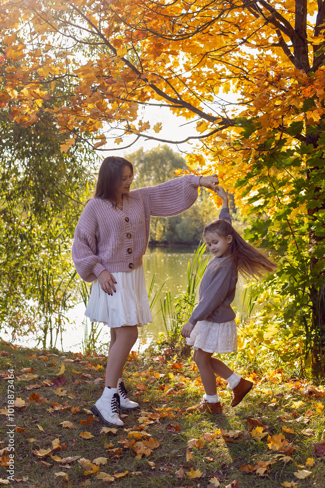 mother and her daughter of seven years walk warm autumn in a park with trees at sunset in orange leaves.