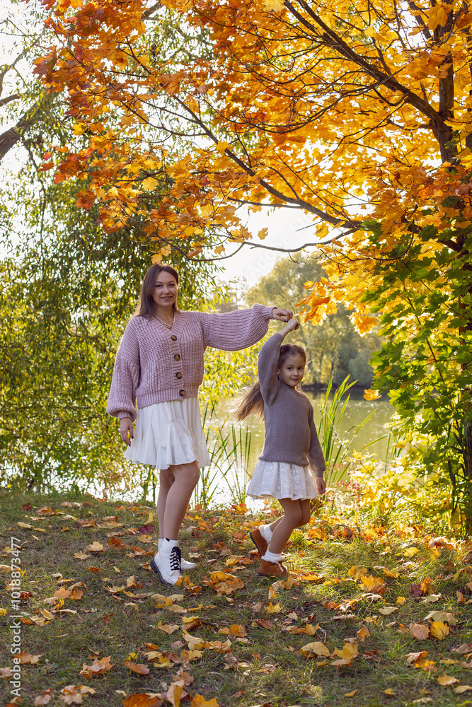 mother and her daughter of seven years walk warm autumn in a park with trees at sunset in orange leaves.