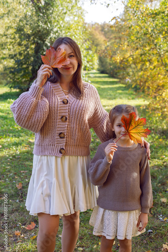 mother and her daughter of seven years walk warm autumn in a park with trees at sunset in orange leaves. cover your face