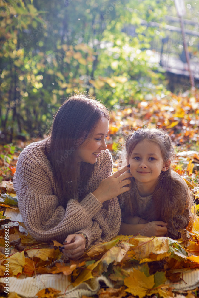 mother and her daughter of seven years walk warm autumn in a park with trees at sunset in orange leaves. lying on the ground among the orange leaves.