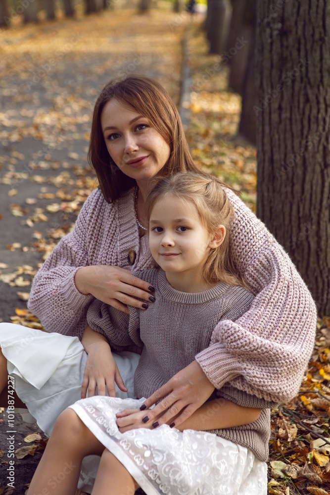 mother and her daughter of seven years walk warm autumn in a park with trees at sunset in orange leaves. sit on the ground among the orange leaves.