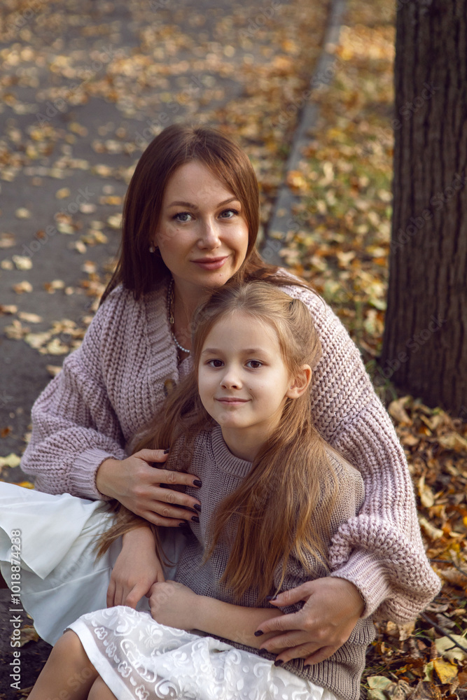 mother and her daughter of seven years walk warm autumn in a park with trees at sunset in orange leaves. sit on the ground among the orange leaves.