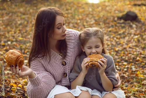 Obraz na płótnie mother and her daughter of seven years walk warm autumn in a park with trees at sunset in orange leaves. sitting on the ground eating croissants. w salonie