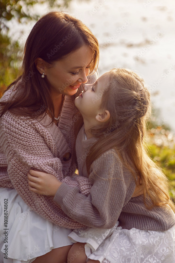 mother and her daughter of seven years walk warm autumn in a park with trees at sunset in orange leaves. sit on the ground among the orange leaves.