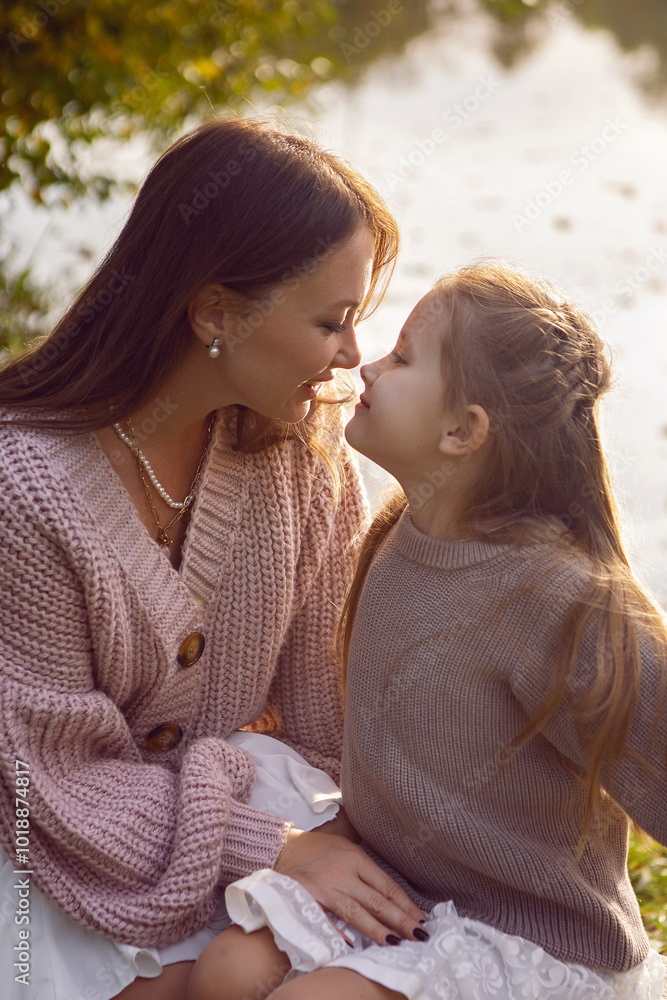 mother and her daughter of seven years walk warm autumn in a park with trees at sunset in orange leaves. sit on the ground among the orange leaves.