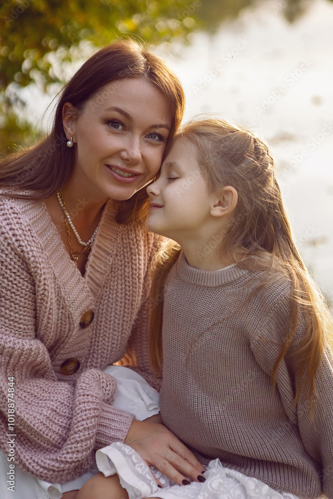 mother and her daughter of seven years walk warm autumn in a park with trees at sunset in orange leaves. sit on the ground among the orange leaves.