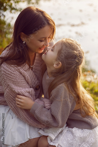 Obraz na płótnie mother and her daughter of seven years walk warm autumn in a park with trees at sunset in orange leaves. sit on the ground among the orange leaves. w salonie