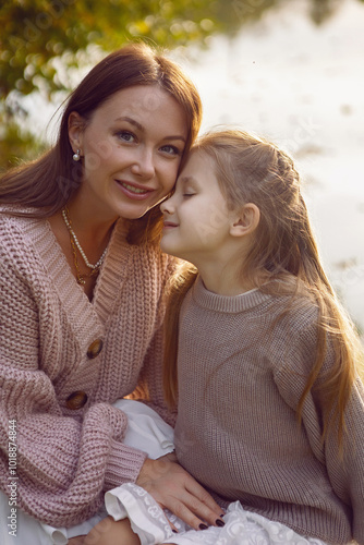 mother and her daughter of seven years walk warm autumn in a park with trees at sunset in orange leaves. sit on the ground among the orange leaves.