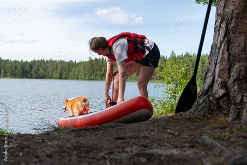 Woman Preparing Paddleboard with Dog by Lake