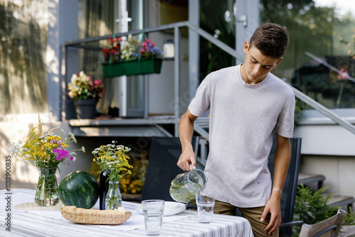 Boy pouring cold tea from jar to glass at table in backyard at day photo