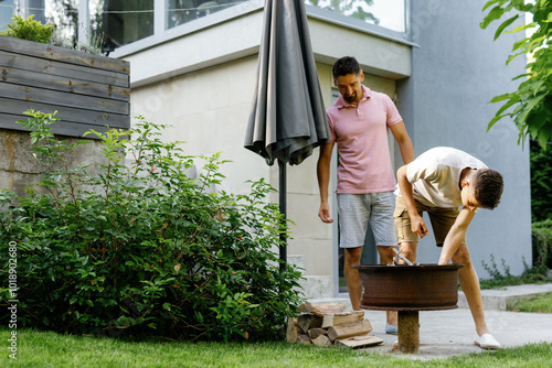 Father looking at son lighting iron grill in backyard of country house photo