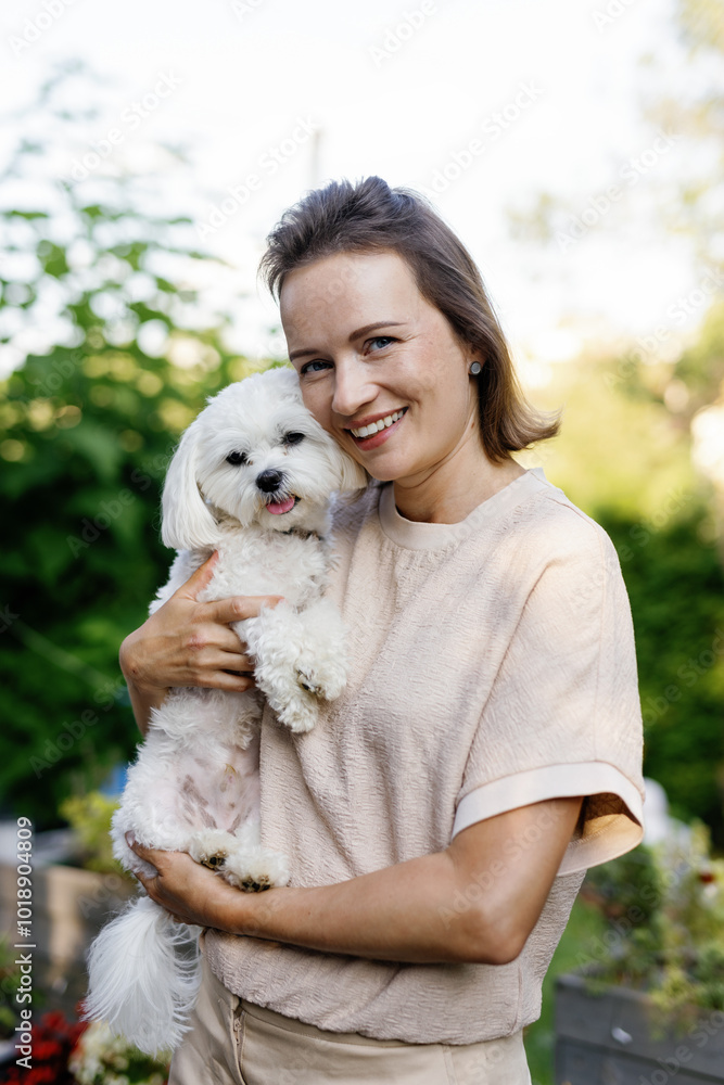 Happy woman with dog in arms looking at camera in blurred backyard Happy woman with dog in arms looking at camera in blurred backyard