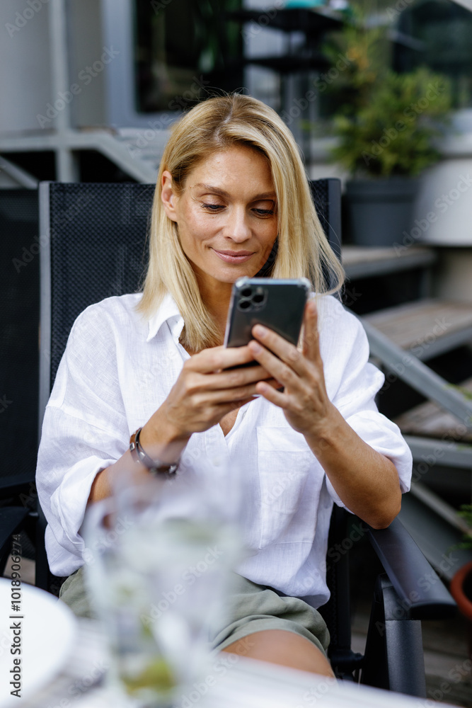 Woman using and watching mobile phone at table on terrace of house Woman using and watching mobile phone at table on terrace of house