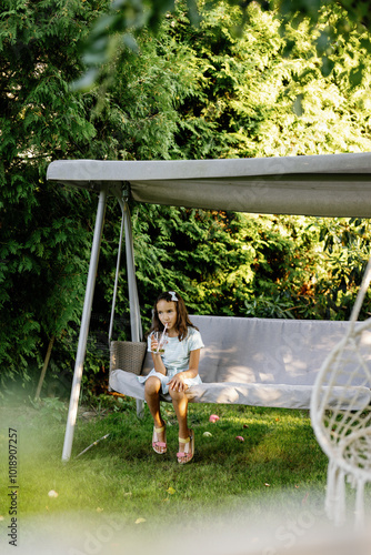 Little girl sitting on porch swing, resting and drinking cold drink photo