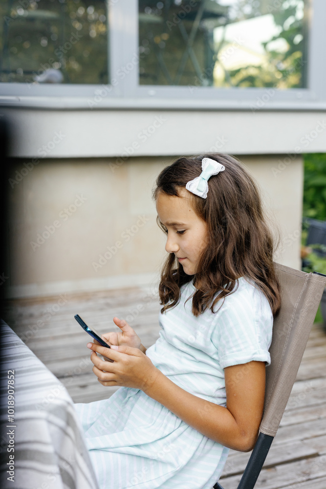 Little girl resting and using smartphone at table on terrace of house Little girl resting and using smartphone at table on terrace of house