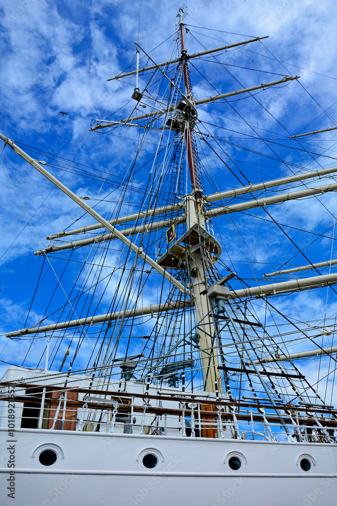 żaglowiec z masztami i olinowaniem, żaglowiec w porcie na tle niebieskiego nieba, Ship Mast and Ropes, ship moored in harbor of coastal town, sailing ship with rigging, Sailing ships moored in harbor